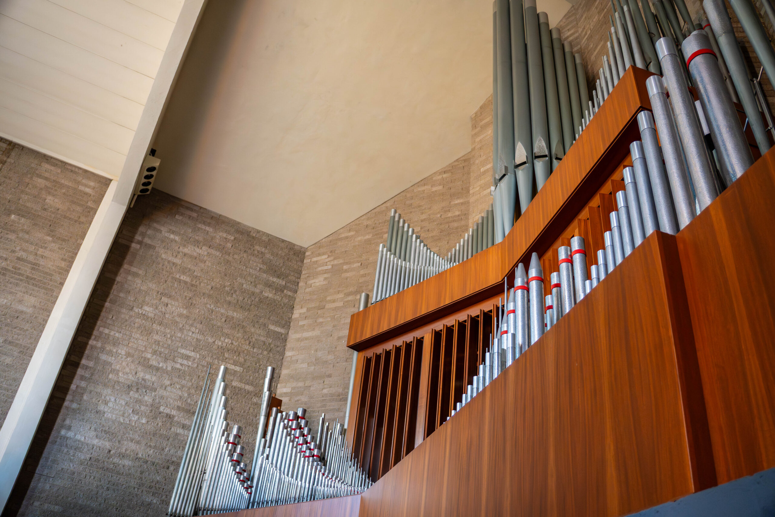 A large church organ with numerous pipes is set against a brick wall and wooden paneling, creating a grand architectural display.