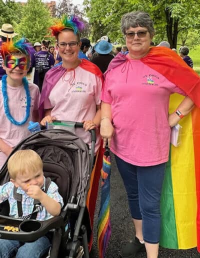 A group of people wearing colorful outfits with a child in a stroller, gathered outdoors, possibly during an event in a park setting.